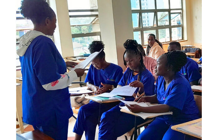 A female medical student in full personal protective equipment, including a blue gown and gloves, with a stethoscope around her neck